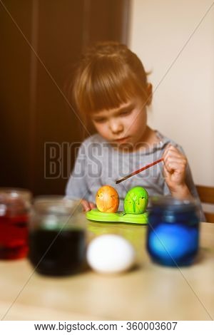 Todder Girl Sitting At The Table And Decorating Easer Eggs With Paint Brush, Vertical Orientation