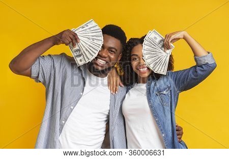 Lucky Black Man And Woman Holding Lots Of Dollar Cash, Covering Faces With Money And Cheerfully Smil