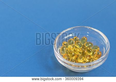 Yellow Gelatin Capsules With Vitamin D3 In A Glass Container On A Blue Background. Pharmaceutical Th