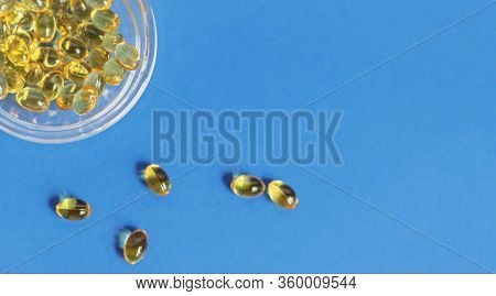 Yellow Gelatin Capsules With Vitamin D3 In A Glass Container On A Blue Background. Pharmaceutical Th