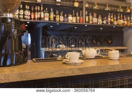 Bar Counter With Cup And White Teapot, Blurred Alcohol Bottles Assortment On Background. Barroom In 