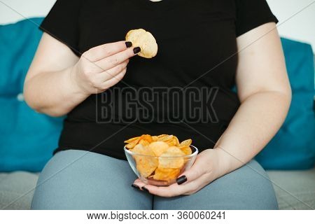 Overeating And Gluttony Concept. Mindless Snacking, Home Sedentary Lifestyle. Obese Woman Sitting On