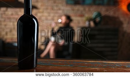 Woman tasting and drinking red wine from wine from elegant wine glass at home in a cosy dark room.