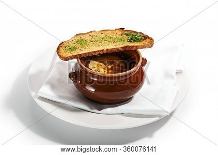 Oven baked meat soup with artichokes in pot. Delicious hot pottage with fresh bread and greenery. Traditional cuisine, restaurant dish, dinner food. Aromatic goulash on white napkin