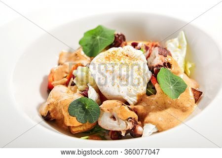 Salad in white bowl. Sliced octopus and fried potato. Served cut ingredients with mayonnaise, tomato spicy ajika and smoked pepper homemade sauce. Restaurant food portion in plate close up