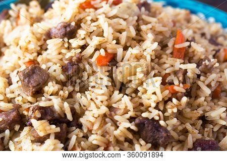 National Cuisine - Uzbek Pilaf With Meat In A Plate With A Traditional Pattern, On A Dark Wooden Tab