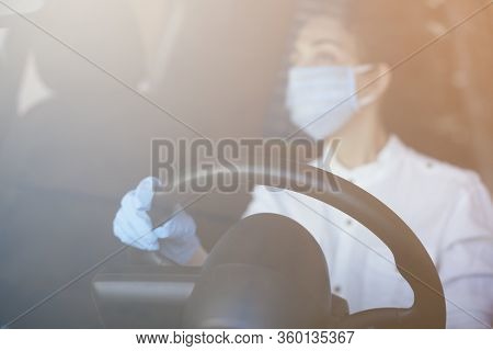 A Young Woman In A Surgical Face Mask And Gloves Driving The Car During Coronavirus Pandemic. A Fema