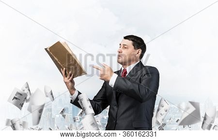 Senior Businessman Finger Pointing Into Open Book. Man In Business Suit And Tie Standing On Cityscap