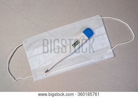 Electronic Thermometer With A Medical Mask On Gray Background