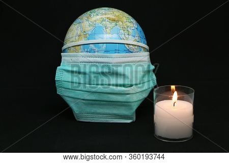 Close-up - A Medical Mask Is Dressed On Planet Earth. A Candle Is Burning Nearby. The Background Is 