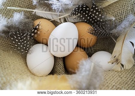 Different Coloured Eggs With Feathers Lying On A Jute Bag