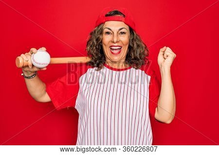 Middle age senior woman wearing baseball equiment, bat and ball over red isolated background screaming proud and celebrating victory and success very excited, cheering emotion