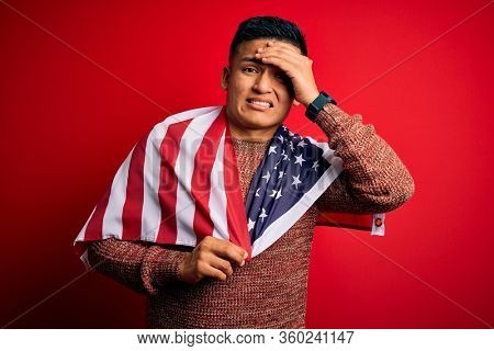 Young handsome latin patriotic man wearing united states of america falg stressed with hand on head, shocked with shame and surprise face, angry and frustrated. Fear and upset for mistake.