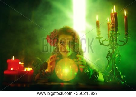 Bewitching fortune teller woman reading future on magical crystal ball.