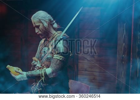 An experienced medieval warrior in armor and with a sword in a wooden house. Stage portrait. The Witcher man.