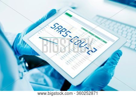 closeup of a doctor man, wearing blue surgical gloves, having a digital tablet in his hands with the text SARS-CoV-2 in its screen