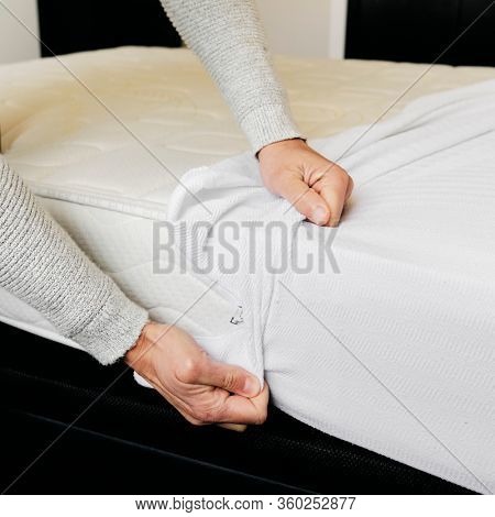 closeup of a young caucasian man covering a mattress with a white mattress protector