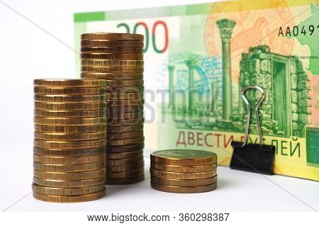 Stacks Of 10-ruble Coins Stand In Front Of A Pack Of Russian Banknotes 200 Rubles. Close-up