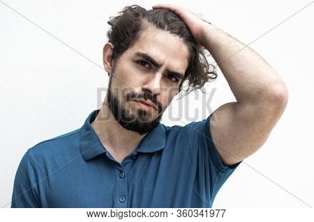 Pensive Attractive Guy Touching Head, Doing Up Hair, Looking At Camera. Handsome Bearded Young Man I