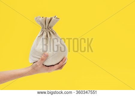 Hand Holds A Textile Bag On A Yellow Background, The Concept Of Money And Financial Assistance, Bank