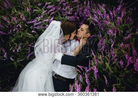 Couple At Sunset In A Wedding Dress Lie On The Grass With Lipin Flowers,festive Spring Wedding Photo