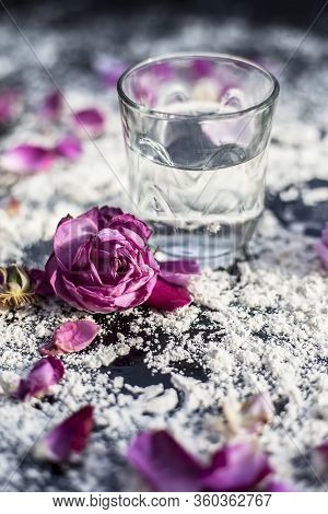 Close Up Shot Of A Glass Of Water Along With Some Rose Petals On A Black Board Spread With Some Whea