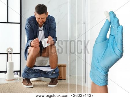 Doctor Holding Suppository For Hemorrhoid Treatment And Man Sitting On Toilet Bowl In Rest Room