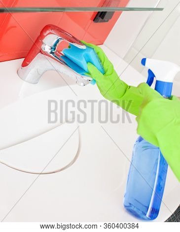 Woman cleaning sink and faucet in bathroom at home