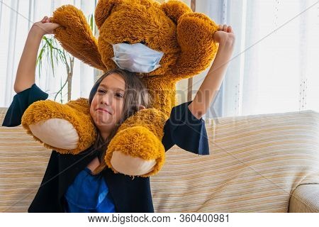 Beautiful Little Girl In A Black Jacket Playing With Her Brown Teddy Bear Who Has Put A Mask To Prot