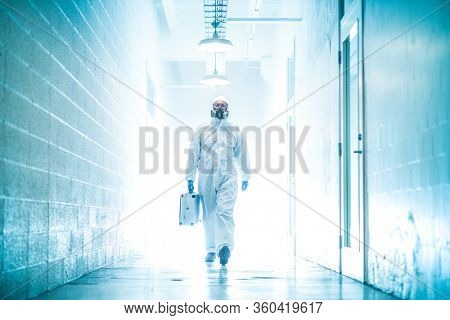 corona virus concept. male scientist doctor in latex biochemical protective suit walking in laboratory coridor holding analysis case with biohazard sign