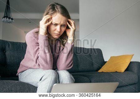 Young Fair-haired Caucasian Woman In Purple Sweater, Grey Home Trousers Sitting On Grey Sofa In Livi