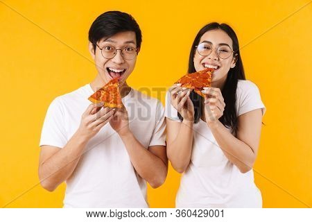 Image of cheerful multinational couple smiling and eating pizza isolated over yellow background