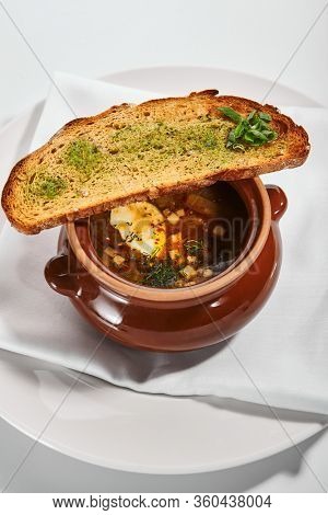 Oven baked meat soup with artichokes in pot. Delicious hot pottage with fresh bread and greenery. Traditional cuisine, restaurant dish, dinner food. Aromatic goulash on white napkin