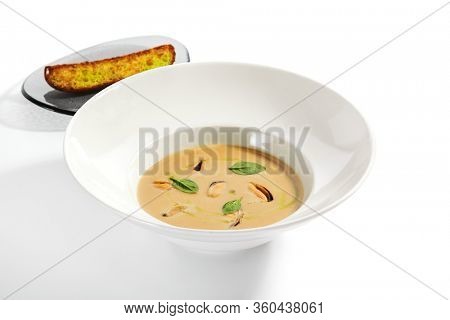 Chilean mussels soup in white bowl. Served main course close up. Seafood cream soup with roasted bread slice. Restaurant food portion, main course with toast. Dinner, gourmet meal in plate