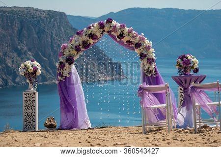 Elegant And Stylish Violet Arch Wedding Ceremony On The Sea. The Round Wedding Arch Is Decorated Wit