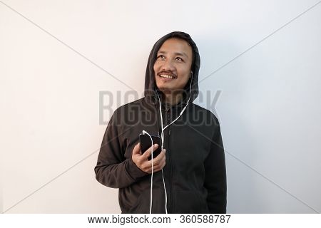 A Man In Hoodie Listening To Music With Headphones From Mobile And Looking At A Blank Copy Space Iso