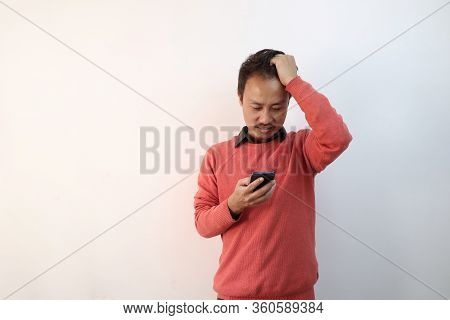 A Man Looking At His Phone Confused And Scratching His Head In Confused Expression Isolated In White