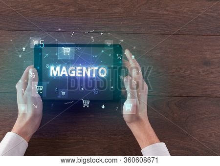 Close-up of a hand holding tablet with MAGENTO inscription, online shopping concept