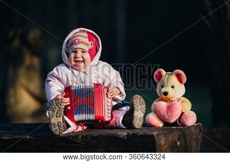 Funny Cute Girl, A Small Child In Fashionable Jeans Plays The Accordion. Happy Baby Plays The Game. 