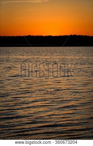 Late Evening River Sunset View With Small Waves On The Water And Orange-yellow Sky. Photo Taken In L