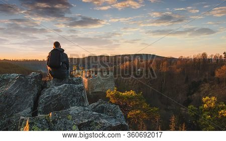Young Man In Jacket, Pants And Backpack Sitting And Looking To Ruin Divci Kamen From Rock. Czech Rep