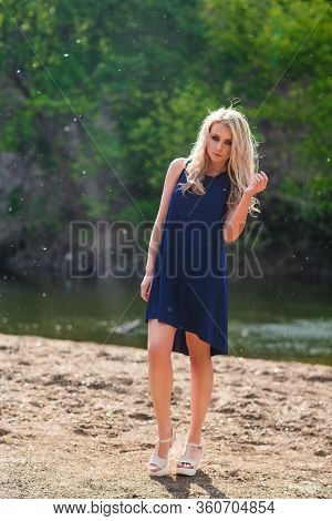 Young Beautiful Blond Woman In Blue Mini Dress And Floral Wreath Standing And Trying Water On Summer