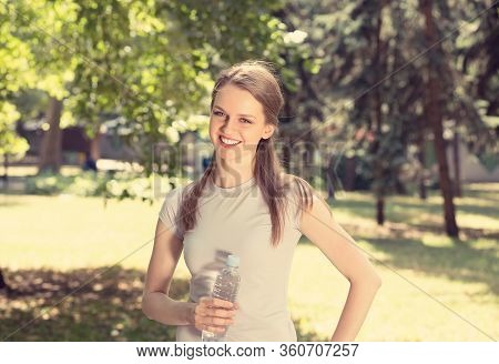 Woman Holding Bottle Of Water In Hands Smiling Looking At You Camera Isolated Green Trees Park Backg