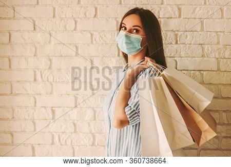Beautiful Girl In Protective Face Mask Holding Shopping Bags In Hands. Young Woman Shopaholic In Med