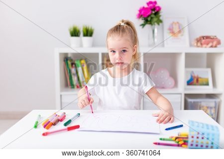 Blonde Happy Little Girl With Ponytale Drawing And Writing Lsitting By The White Table In Light Roon