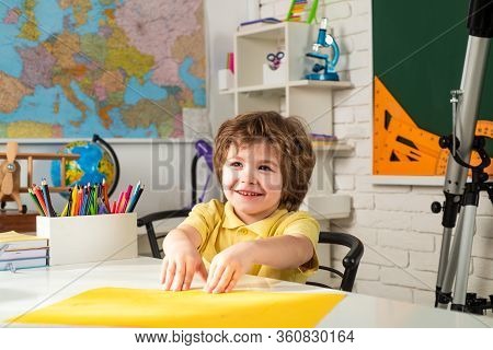 Happy Cute Industrious Child Is Sitting At A Desk Indoors. Children Learning. Little Children At Sch