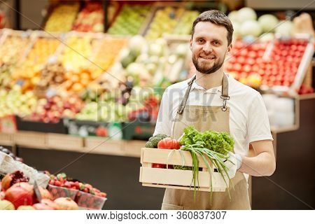 Waist Up Portrait Of Bearded Man Holding Box Of Vegetables And Smiling At Camera While Selling Fresh