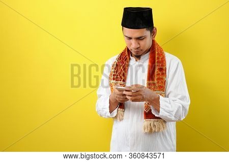 Young Asian Muslim Man Wearing Moslim Clothes Holding Mobile Phone Look At Phone Screen, Isolated On