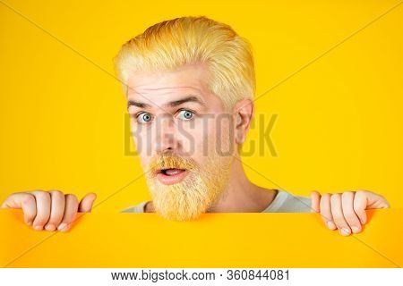 Young Man Shows A Sheet Of Paper In The Camera On A Yellow Background. Male Model Holding White Boar