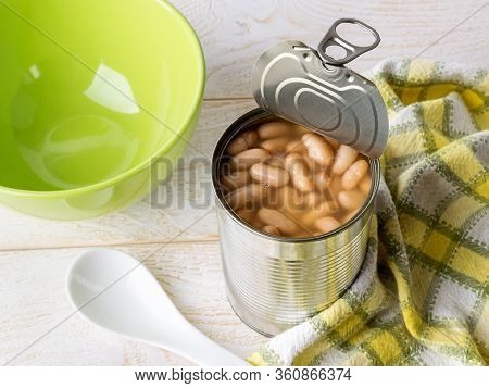 Canned Backed Beans In An Open Tin Can With Pull Tab Near Ceramic Bowl And Spoon On A Wood Table. Be